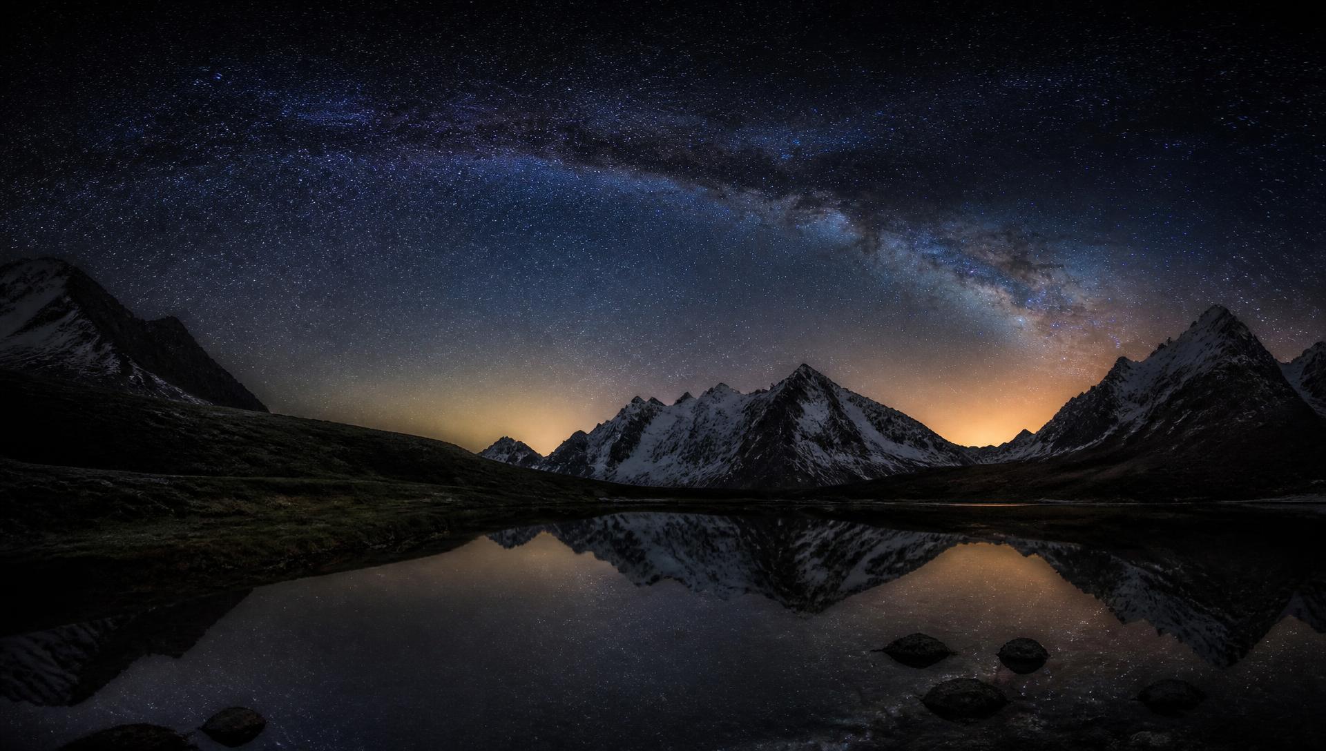 Cielo estrellado sobre una cordillera reflejada en un lago en calma